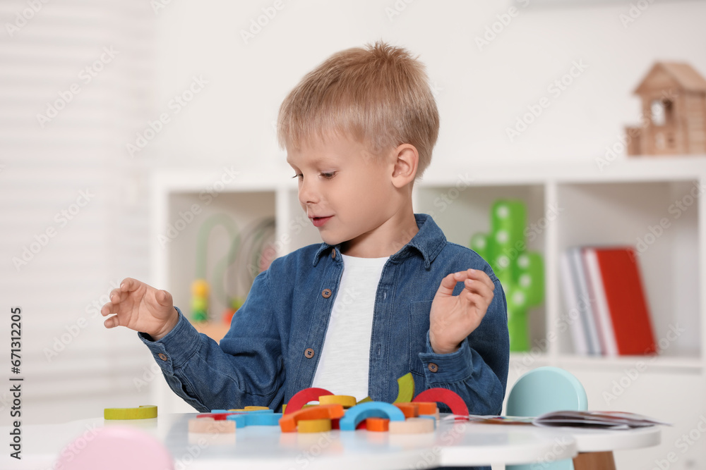 Wall mural Cute little boy playing with colorful wooden pieces at white table indoors. Child's toy