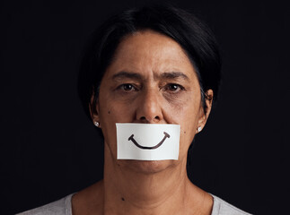 Portrait, fake smile or abuse and a mature woman in studio on a dark background with an expression....