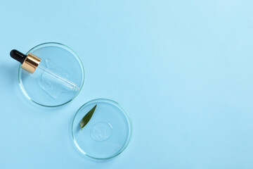 Petri dishes with samples of cosmetic oil, pipette and green leaf on light blue background, flat...