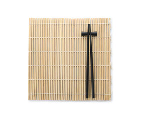 Bamboo mat with pair of black chopsticks and rest isolated on white, top view