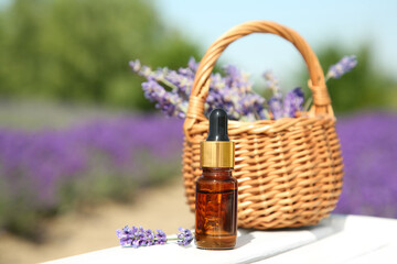 Fototapeta na wymiar Bottle of essential oil and wicker bag with lavender flowers on white wooden surface outdoors, closeup