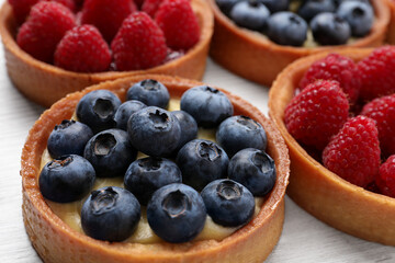 Tartlets with different fresh berries on white table, closeup. Delicious dessert