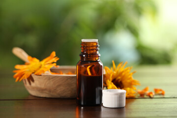 Bottle of essential oil with calendula extract on wooden table outdoors, closeup