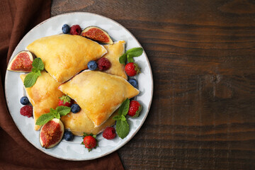 Delicious samosas with figs and berries on wooden table, top view. Space for text
