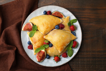 Delicious samosas with figs and berries on wooden table, top view