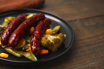 Delicious smoked sausages and baked vegetables on wooden table, closeup