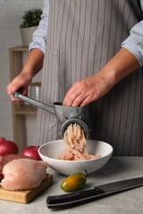 Woman making chicken mince with metal meat grinder at grey table indoors, closeup