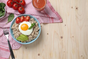 Delicious boiled oatmeal with fried egg, bacon, avocado and tomato served on wooden table, flat lay. Space for text