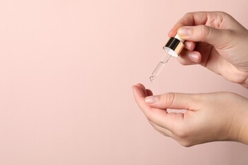 Woman applying cosmetic serum onto fingers on light pink background, closeup. Space for text
