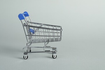 Small metal shopping cart on light background, space for text