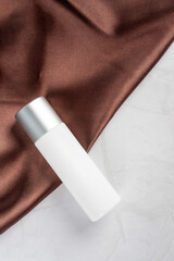 Cosmetic bottles made of dark amber glass on shiny cloth background