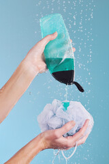 Woman, hands and loofah with soap in shower for hygiene, washing or cleaning body against a blue studio background. Closeup of female person pouring gel bottle with falling water or rain on sponge