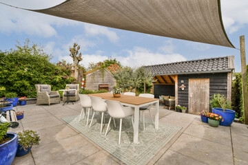 a patio area with chairs, tables and an umbrella over the dining table in front of a wooden shed...