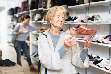 Fototapeta na wymiar Senior woman standing at shelves in shoe store and choosing new running shoes.