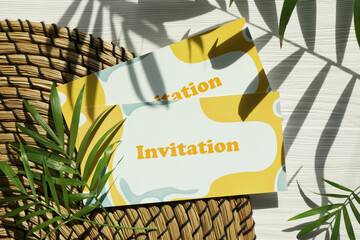 Beautiful cards with word Invitation and palm leaves on white wooden table, flat lay