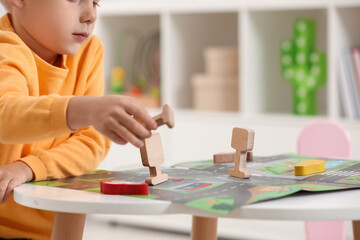 Little boy playing with set of wooden road signs and cars at table indoors, closeup. Child's toy