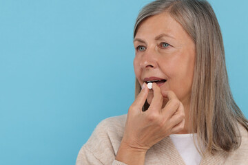 Senior woman taking pill on light blue background. Space for text