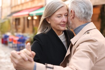 Fototapeta na wymiar Affectionate senior couple dancing together on city street