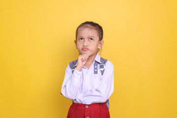 Thoughtful Asian elementary school girl wearing uniform and backpack looking up and showing serious thinking expression