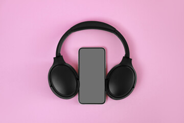 Modern wireless headphones and smartphone on pink background, top view