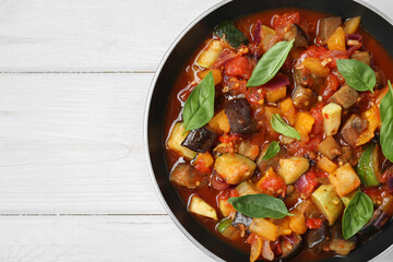 Frying pan with tasty ratatouille on white wooden table, top view. Space for text