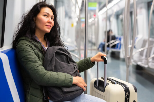 Young adult woman passenger with luggage sitting in subway car