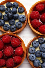 Tartlets with different fresh berries on white wooden table, flat lay. Delicious dessert