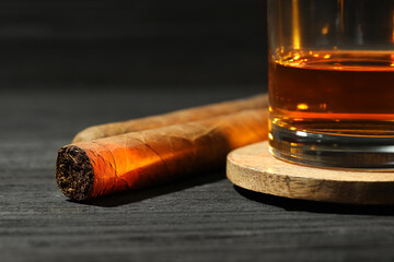 Glass of whiskey and cigars on black wooden table, closeup