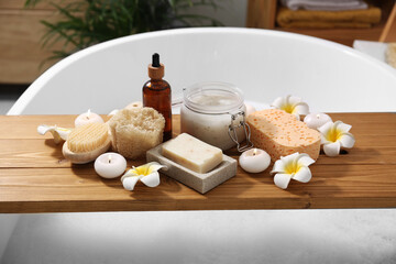 Composition with different spa products and beautiful flowers on tub tray in bathroom