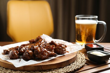 Tasty chicken wings, sauces and mug of beer on wooden table, space for text. Delicious snack
