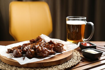 Tasty chicken wings, sauces and mug of beer on wooden table, space for text. Delicious snack