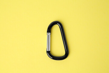 One black carabiner on yellow background, top view - obrazy, fototapety, plakaty