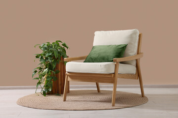 Stylish armchair with cushion and green plant near beige wall indoors
