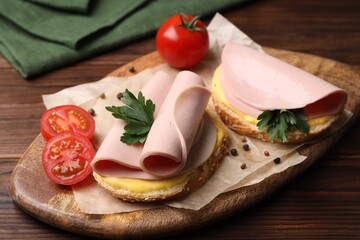 Delicious sandwiches with boiled sausage, cheese and tomatoes on wooden table, closeup