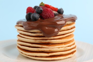 Stack of tasty pancakes with fresh berries and chocolate spread on light blue background, closeup