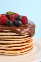 Stack of tasty pancakes with fresh berries and chocolate spread on light blue background, closeup