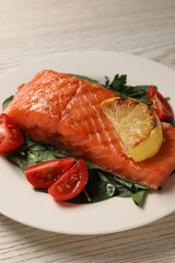 Tasty grilled salmon with tomatoes, lemon and basil on white wooden table, closeup