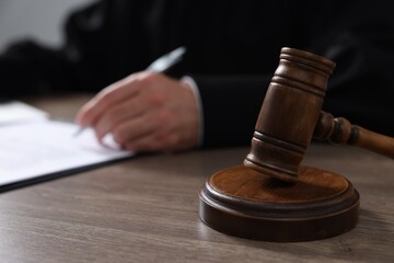 Judge with gavel writing in papers at wooden table, closeup