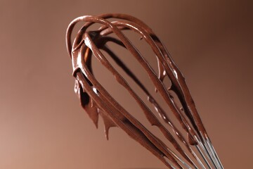 Chocolate cream flowing from whisk on brown background, closeup