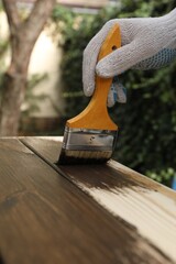 Man applying wood stain onto wooden surface outdoors, closeup