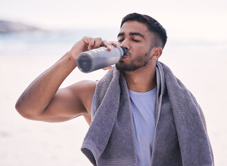 Fitness, sports and man drinking water at the beach after running, training or morning cardio workout with bottle. Exercise, break and thirsty Indian male runner or person with hydration drink at sea