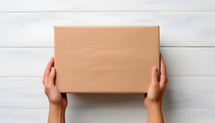 Top view of beige parcel cardboard box in a man hands with blank space on light white wooden surface. Messenger and delivery service concept.