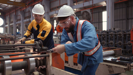 A team of factory technician use a wrench to inspect the conveyor belt of the metal sheet...