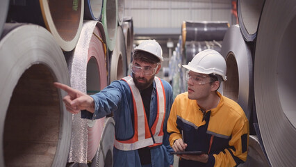 A team of young men working in a warehouse storing rolls of metal sheets. Inspecting the metal sheet rolls stored in the warehouse to be imported onto the metal sheet production line.