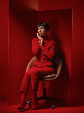Fashion, thinking and a model woman on a red background in studio for elegant, chic or trendy style. Aesthetic, art and confident beauty with edgy or classy young person in unique clothes on a chair