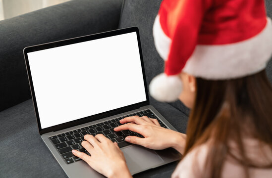 Woman wearing red Christmas hat and hand type on the keyboard on laptop with mockup of blank screen for the application.