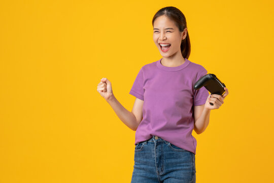 Happy smiling young woman play gaming with a joystick on yellow background.