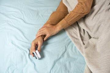 Female's hands with a pulse oximeter at the index finger. Woman lying at the bed. Gadgets for...