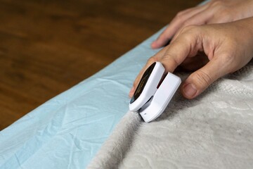Female's hands with a pulse oximeter at the index finger. Woman lying at the bed. Gadgets for...