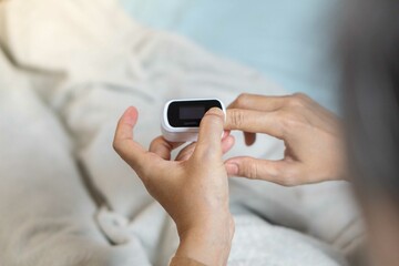 Female's hands with a pulse oximeter at the index finger. Woman lying at the bed. Gadgets for health care. Concept of determination of oxygen in the blood. SHOTLISThealth